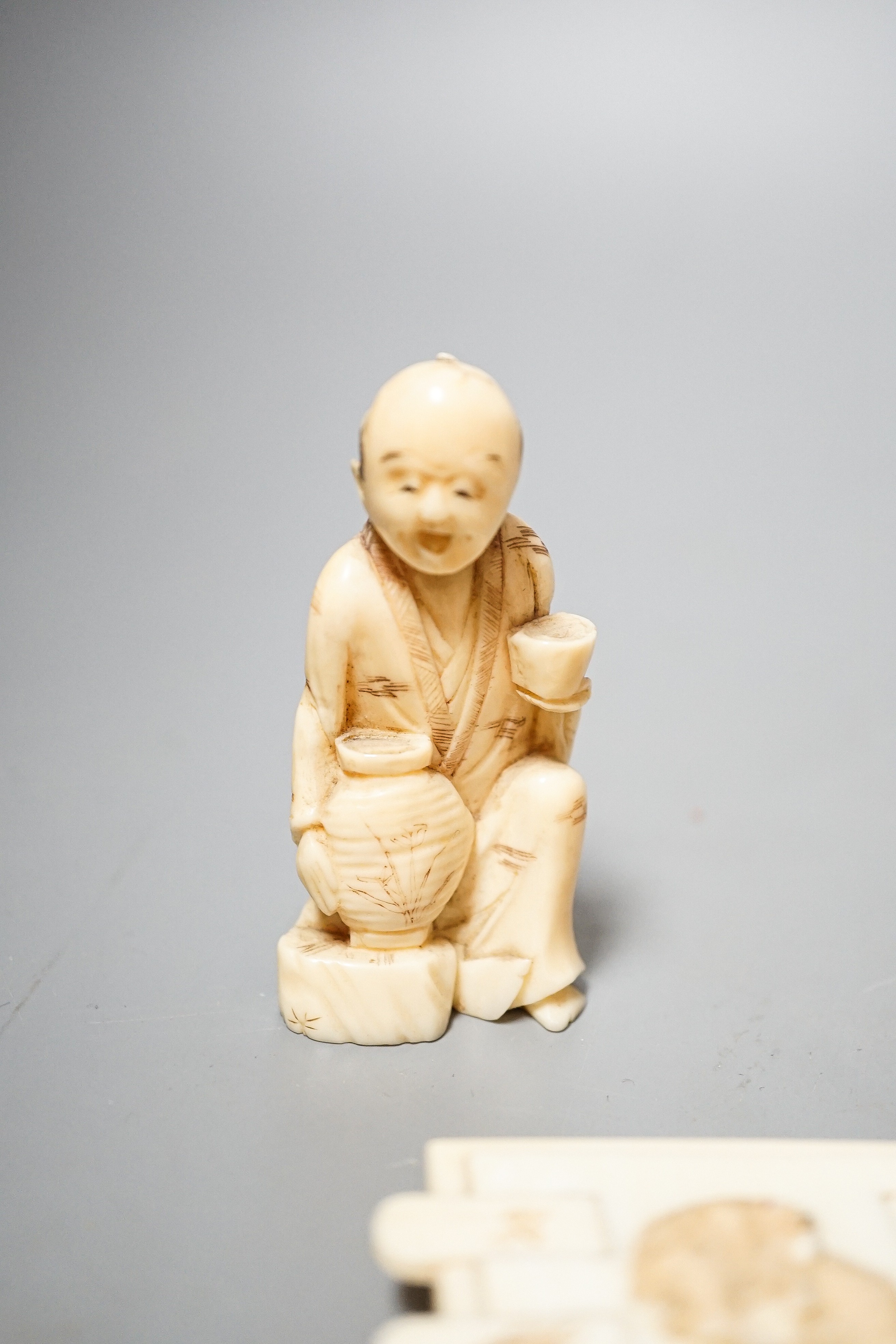 Three Japanese Ivory figures of men, a similar bezique marker, a Japanese staghorn single section inro with ivory manju, a Chinese ivory carving and a bone needlework container